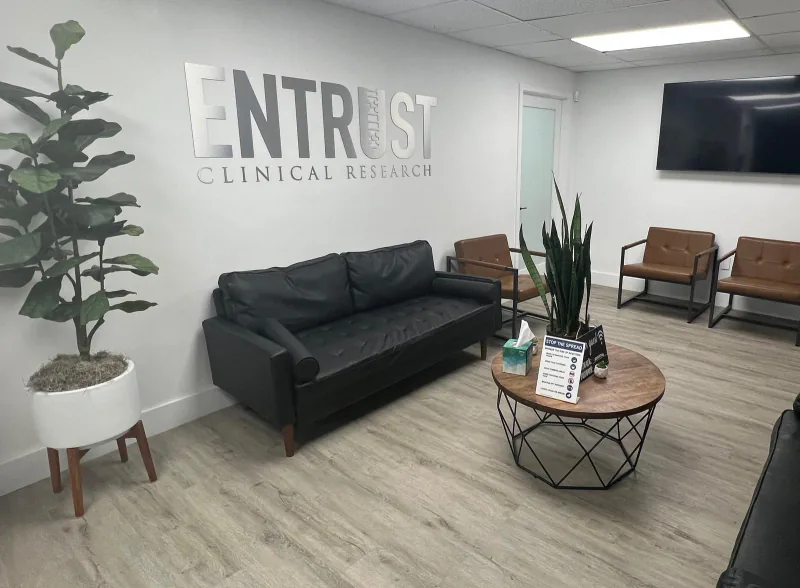 Entrust Clinical Research lobby with the wall sign above a black sofa, brown chairs, and a round coffee table